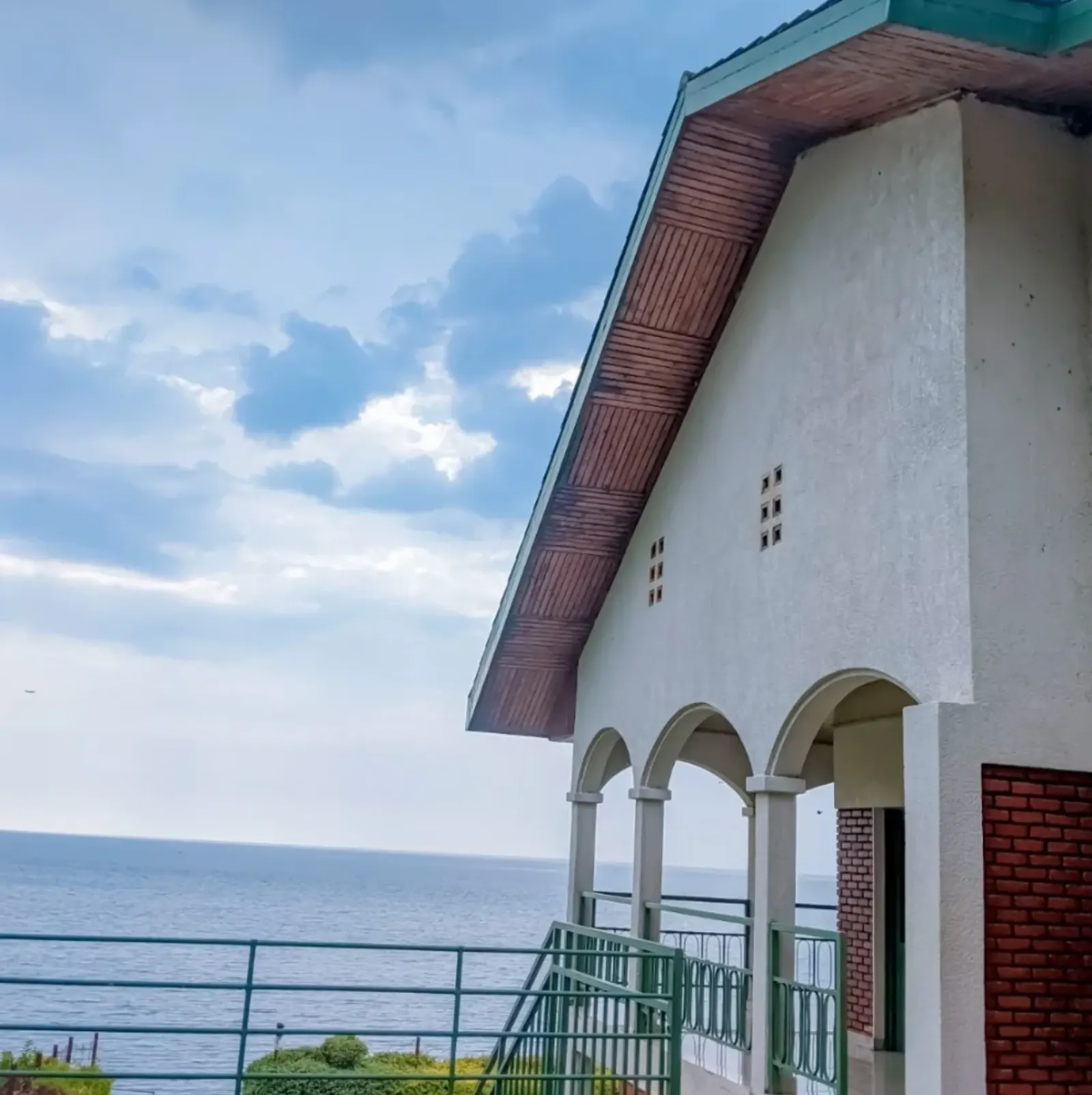 A white house with arched verandas overlooking the open water of Lake Kivu